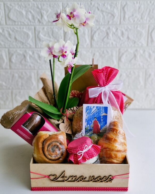 Cesta Amo Você 2 Cesta de café da manhã romântica em caixa de MDF decorada com o letreiro de madeira 'Amo você' preso por um cordão rosa. A composição exibe uma orquídea branca com miolo roxo, uma foto personalizada revelada, croissant amanteigado, rolinho de canela, pão rústico de fermentação natural, um pote de geleia com tampa de tecido poá rosa, um pacote de tecido combinando e uma caixa de doce. Opção de presente afetivo e romântico em São Gonçalo.