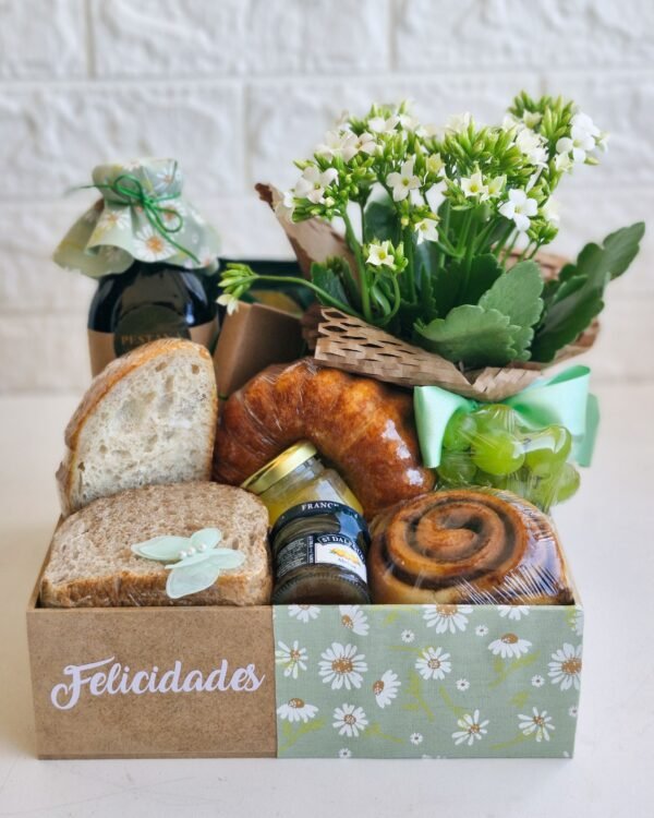 Cesta Gratidão 3 Cesta de café da manhã em caixa de MDF decorada com tecido floral verde claro com estampa de margaridas e adesivo branco de felicitações. Contém uma seleção farta de pão rústico, pão integral, bolo caseiro, geleia de damasco, rolinho de canela, uvas frescas, suco com tampa de tecido combinando e flor Kalanchoe branca.