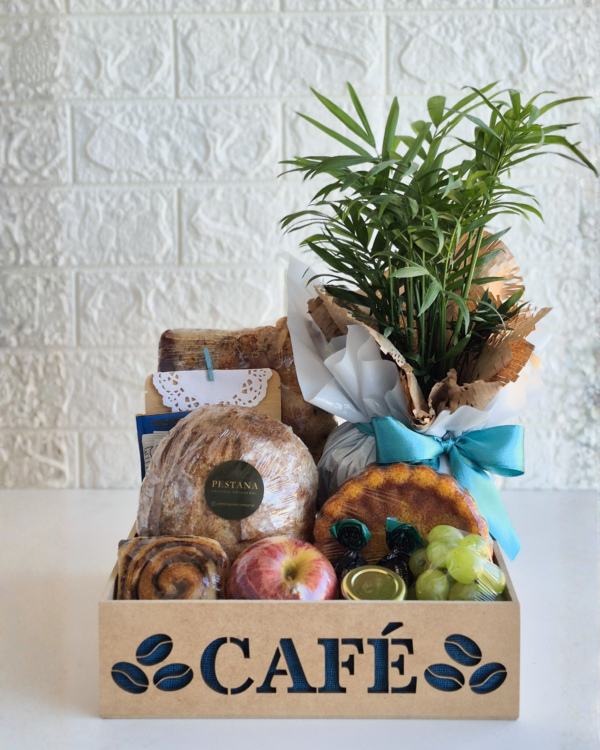 Cesta Café 2 Cesta de café da manhã em caixa de madeira com a palavra vazada "CAFÉ". Composição inclui pão rústico redondo de fermentação natural com adesivo da Pestana, minibolo caseiro, rolinho de canela, frutas frescas (maçã e uva), bombons trufados e um lindo vaso de planta palmeira-chamaedorea embalado para presente.